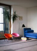 Farbige Retrosessel und blauer Diwan im minimalistischen Wohnraum