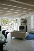 Offener Wohnraum mit gemütlichem Sofa unter weiss lackierter Holzdecke