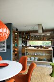 Chairs with orange upholstery in dining area in front of open-plan kitchen with island