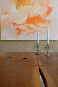 Two candlesticks with blue candles on solid wooden table in front of modern painting on wall