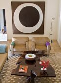 Hand-made, artistic coffee table and modern, sand-coloured sofa set in front of modern painting on wall