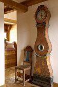 Antike Standuhr mit geschwungenem Gehäuse und alter Holzstuhl in renoviertem, rustikalem Altbau