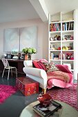 XXXL chair in front of bookshelves and modern art above an old writing table -- living room with red and pink carpets and accessories