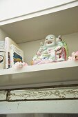 Laughing, Buddha made of Chinese porcelain next to books in a bookshelf