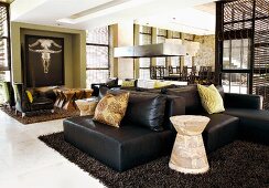 Modern, open living room with black leather sofas and chairs and ethnic South African elements