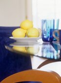 Zitronen auf Teller neben farbigen Wassergläsern auf Tisch