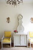 Baroque armchairs with yellow covers next to white-painted longcase clock on cabinet
