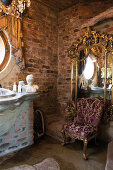 Elegant rococo armchair in front of gilt-framed mirror on brick wall of bathroom