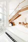 White, shiny piano in a split level living room with open designer stairs in front of floor-to-ceiling windows