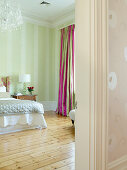 Pale green bedroom with simple wooden floor and colourful curtains with pink stripes