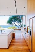 Minimalist designer kitchen in front of open, panoramic glass wall with sea view