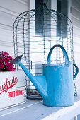 Vintage watering can in front of a bird cage on a wooden table