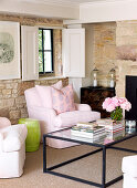 Glasplatte auf Couchtisch vor eleganten rosa Sessel mit Kissen in rustikalem, modernisierten Wohnzimmer mit Natursteinwand