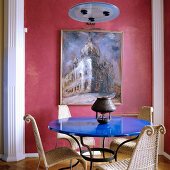 Runder Tisch mit blaulackierter Platte und Stühlen aus Rattan in traditionellem Wohnzimmer mit hellroter Bemalung an Wand