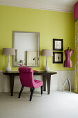 Wohnzimmer im Art-Deco-Stil - Polsterstuhl mit pinkfarbenem Stoffbezug vor Wandtisch mit eleganten Tischlampen an gelb getönter Wand