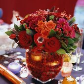 Bouquet in various shades of red in matching glass vase with red decorative beads