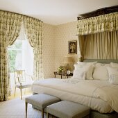Traditionelles Schlafzimmer mit gepolsterten Hockern vor Doppelbett und Baldachin