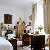 Antique desk in bedroom in front of window with floor-length, gathered curtains