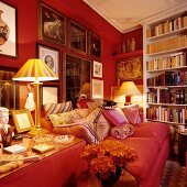 Corner of traditional living room with red sofa against red wall with framed pictures