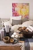Birds' nests and wooden bowl of decorative items on rustic coffee table in front of black and white sofa and picture of candles and roses