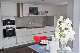 White lilies on dining table in front of white, designer fitted kitchen