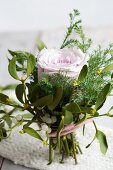 A small bouquet of a rose, mistletoe and conifers