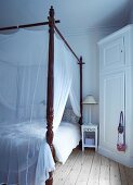 Antique four-poster bed with airy fabric canopy in rustic bedroom