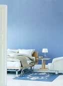 Nachttisch neben Bett und modernem Sessel vor blau getönter Wand