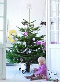 Child sitting on floor in front of decorated Christmas tree