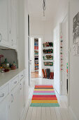 Narrow hallway with white fitted cupboard and multi-coloured rug on white wooden floor