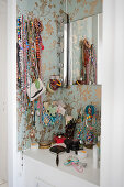Open jewellery racks hanging over dressing table on bedroom wall with wallpaper patterned with gold floral design