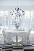 Designer pendant lamp above dining table and white chairs on black and white striped rug