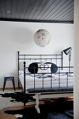Antique-style metal bed and cow-skin rug below black-painted wooden ceiling and Japanese paper lampshade