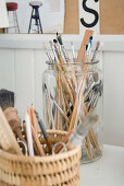 Glass jar and basket of various paintbrushes and writing utensils