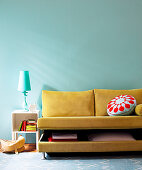 Yellow-brown sofabed with half-opened bedding box combined with table lamp and wall in complementary colours
