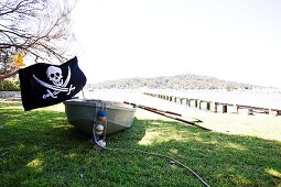 Rowing boot with skull and crossbones flag on grass of lake shore