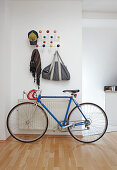 Coat rack made of white wire with colourful spherical hooks above racing bike in open-plan, modern hallway