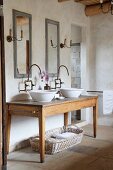Twin wash basins on rustic wooden table and improvised wall-mounted taps below vintage-effect mirrors