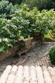 View across porch roof of stone bench against stone wall in Mediterranean garden