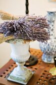 Dried lavender flowers and twigs resting on antique Greek vase on side table with perforated wooden top