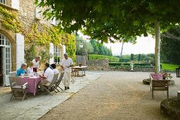 Gäste beim Frühstücken auf grosszügiger Terrasse vor Landhaus und Blick in mediterranen Garten