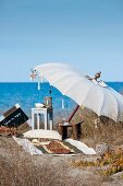 Seaside idyll - beach towel and stool on sandy ground below open parasol beside the sea