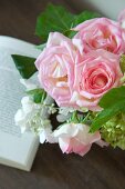 Zarter rosaroter Rosenstrauss und geöffnetes Buch auf Holzunterlage