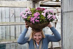 Frau hält lachend eine große Blumenschale auf dem Kopf
