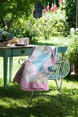Patchwork blanket with delicate patterns draped over garden chair in front of old wooden table in summer garden