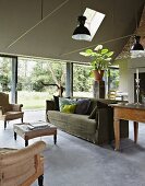 Sofa and armchairs in smoking room with walls painted khaki green, concrete floor and glass wall with view of garden