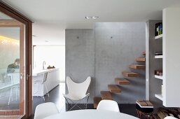 View from dining area of butterfly chair and cantilever wooden steps on exposed concrete wall; white kitchen counter in background