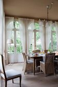 Wicker chairs around breakfast table in front of arched French windows in dining room with traditional ambiance