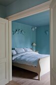 Blick durch offene Tür in himmelblaues Schlafzimmer mit Doppelbett in ländlichem Stil