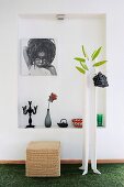 Home-made coat rack and rattan stool in front of photograph hanging in niche